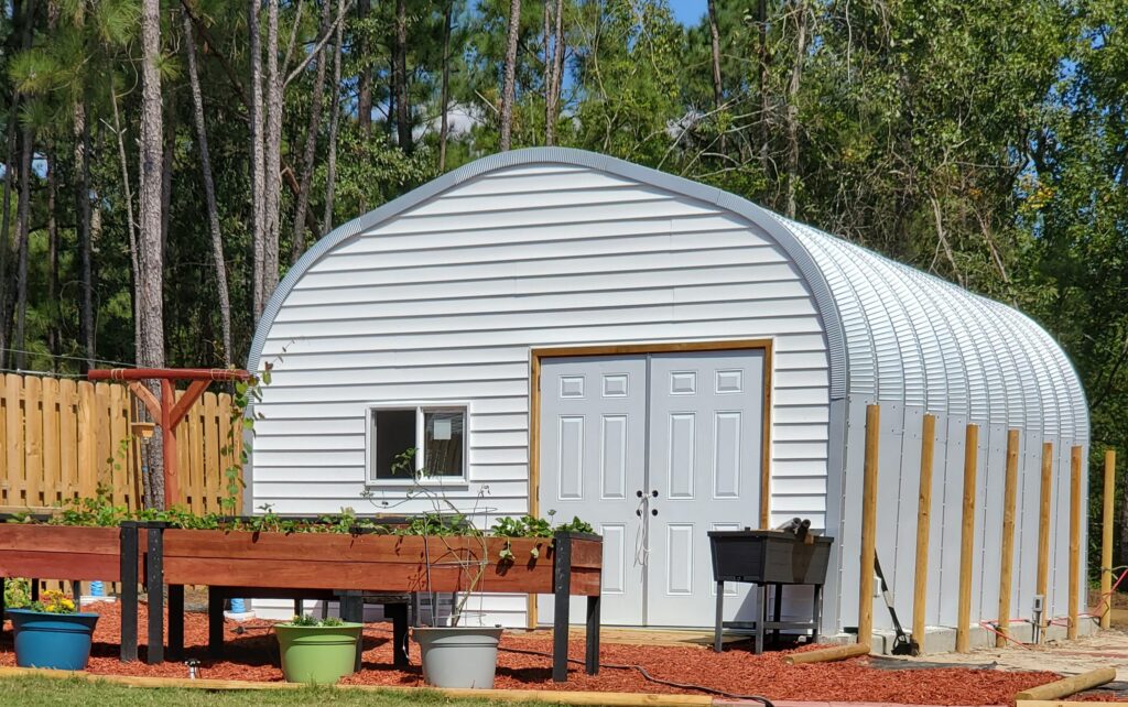 white siding custom front endwall of an A model steel shed with white walk through doors and a garden in front