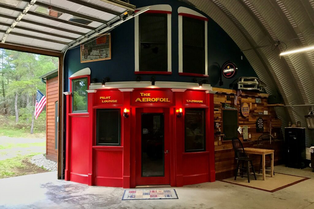 Bar lounge inside of metal quonset hut wtih red and wood facade with guinness sign and table and chairs